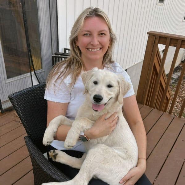 Woman smiling with adorable golden retriever puppy on a wooden deck.