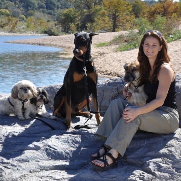 Woman with four dogs sitting on rocks by a lake during fall, enjoying outdoor pet care.