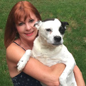 Woman smiling and holding a white and black dog outdoors on green grass.