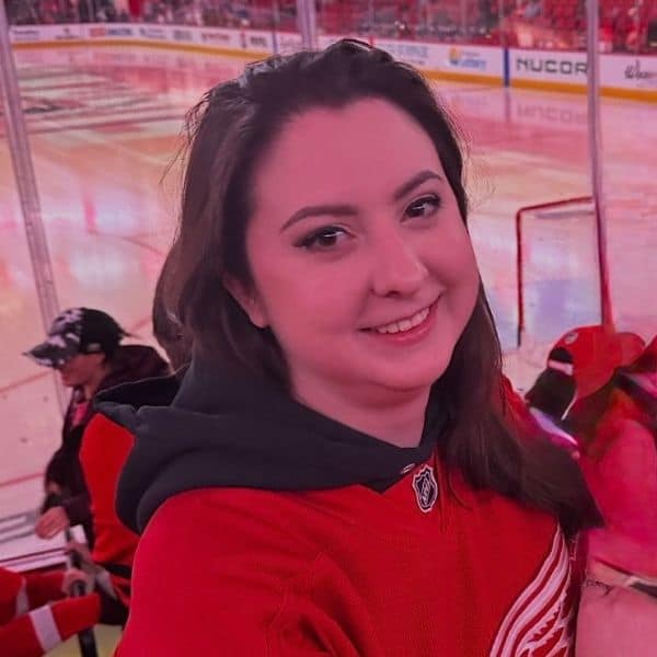 Hockey fan smiling at the rink, wearing a red jersey and enjoying the game.