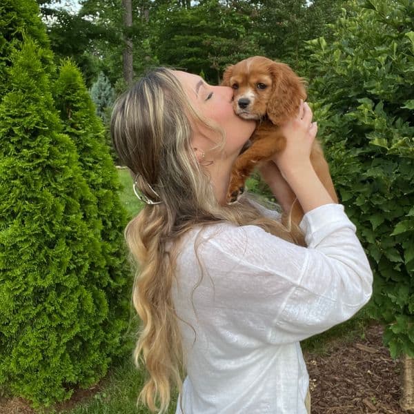 Pet owner kissing cute puppy outdoors in lush garden setting.